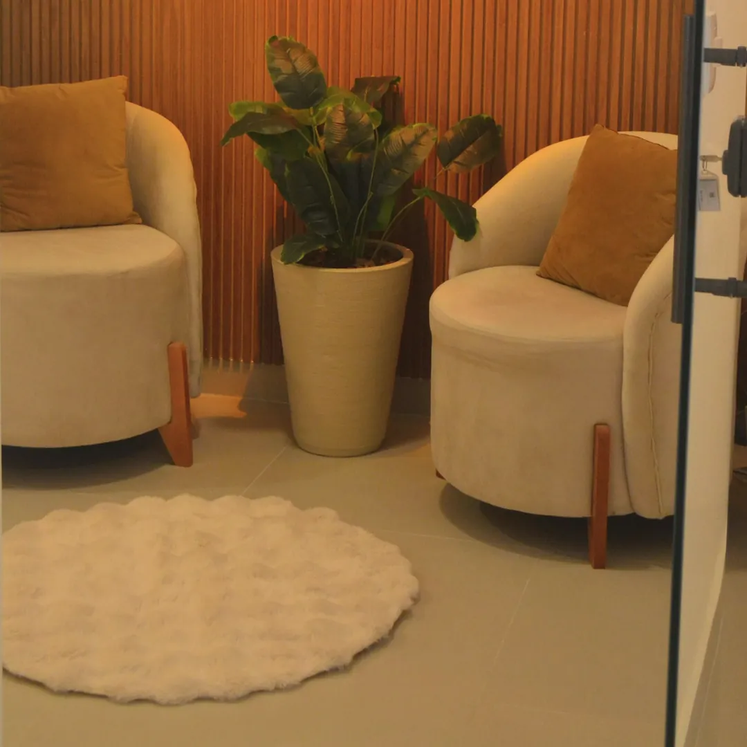 Rincón de espera con dos sillones color crema, una planta y una alfombra.